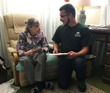 A young adult reads to a person sitting on a couch