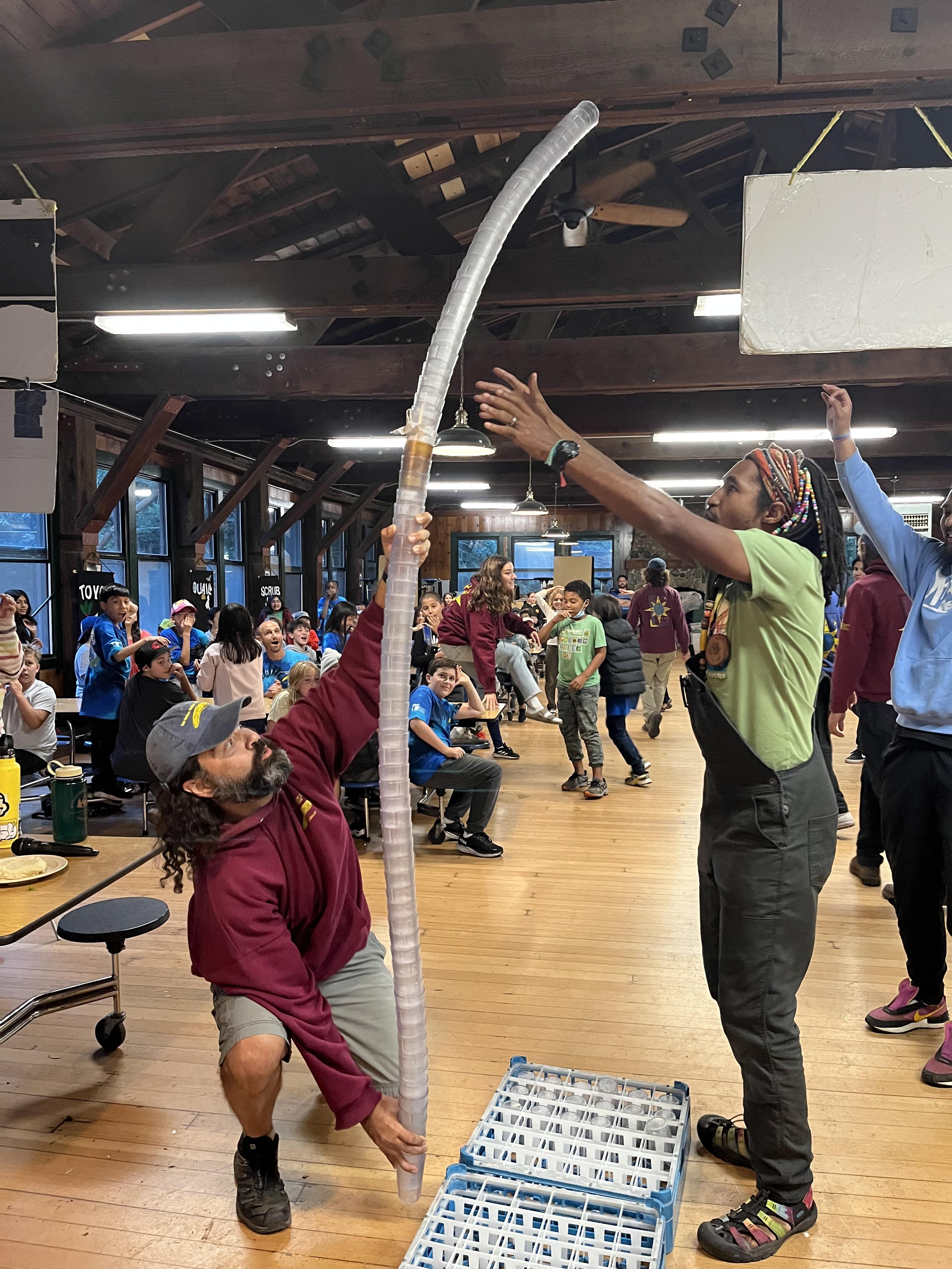 Two naturalists stack a bunch of cups to make a giant tower with students looking on.