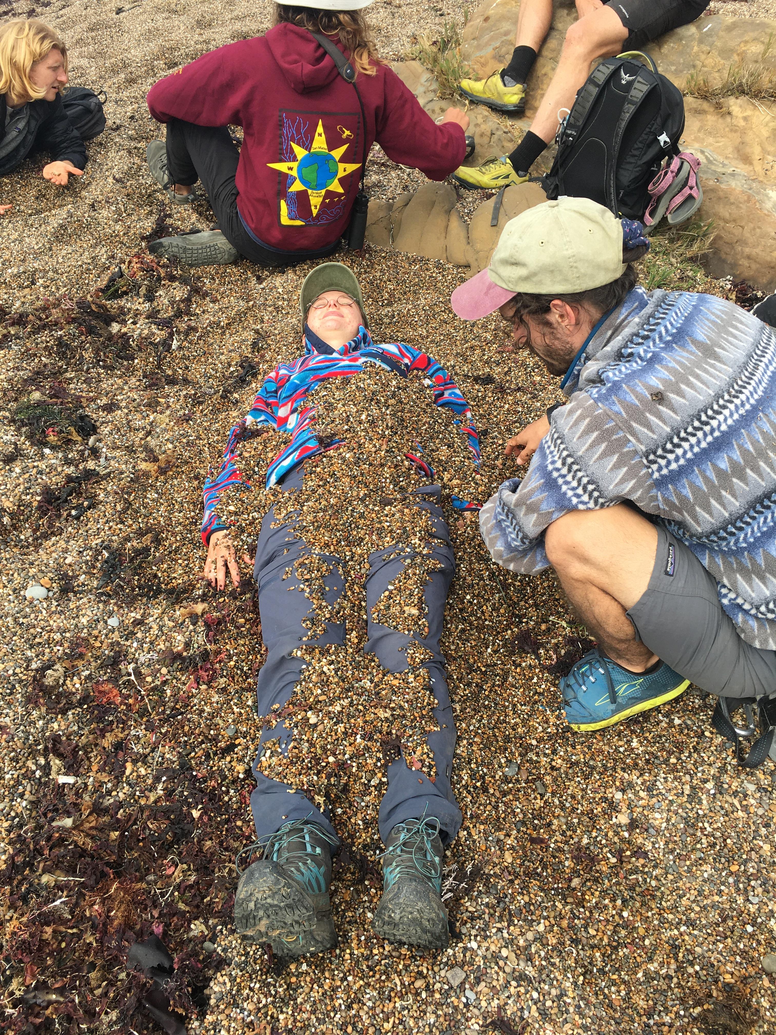 A person buried in pebbles with other people around them