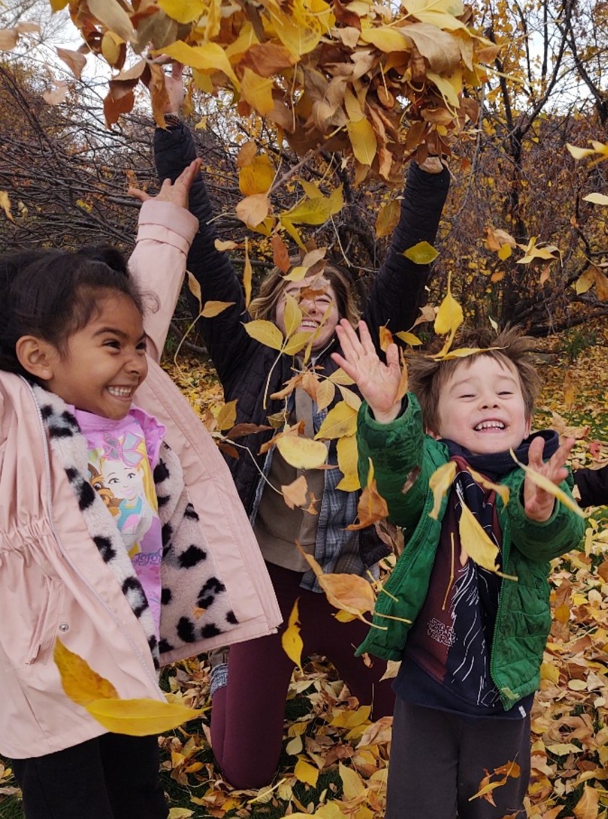 A Thorne AmeriCorps educator and two students throw leaves in the air and smile