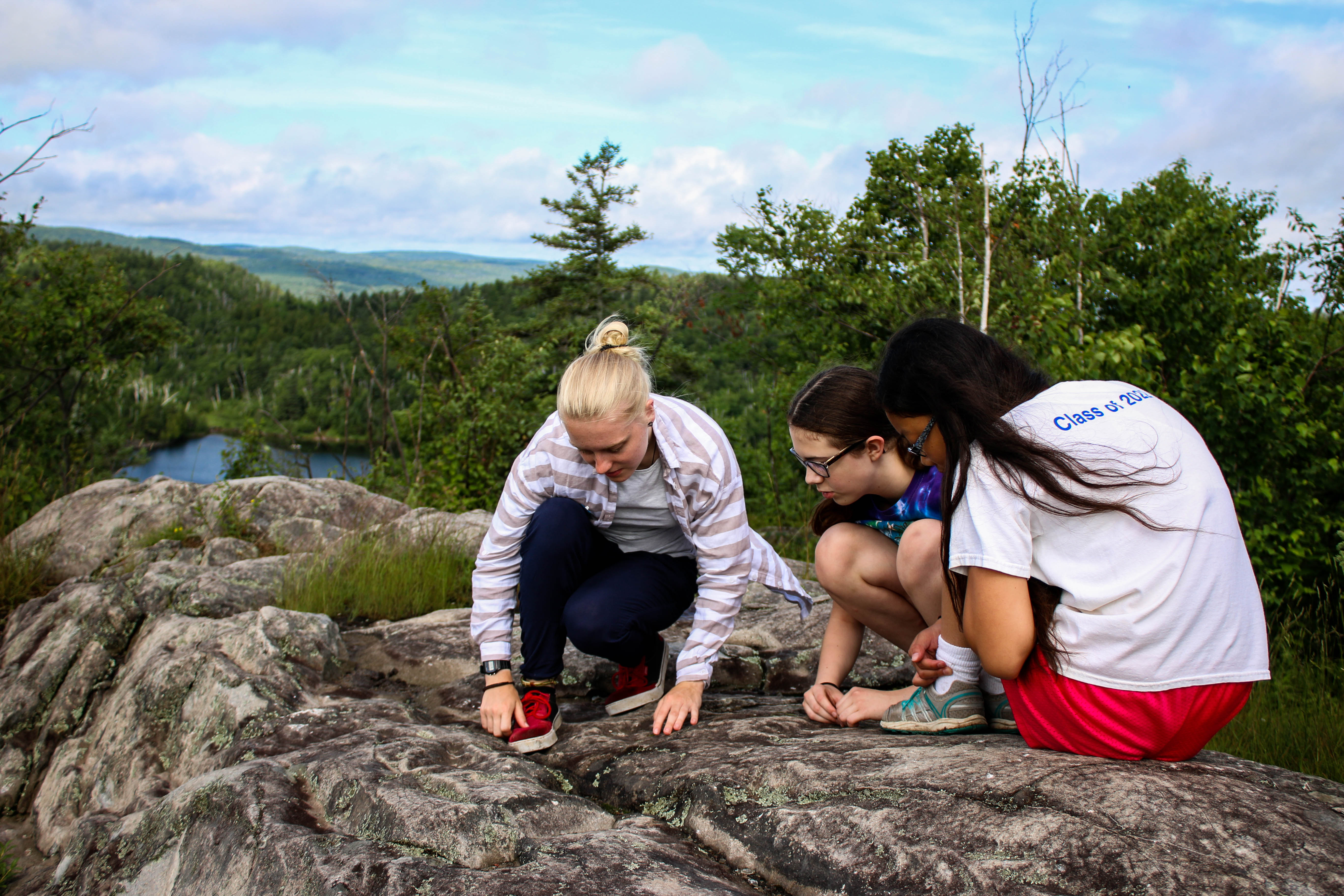 A camp counselor shows a group of campers some lichens up on top of Marshall Mountain overlooking Wolf Lake on the Wolf Ridge Campus.